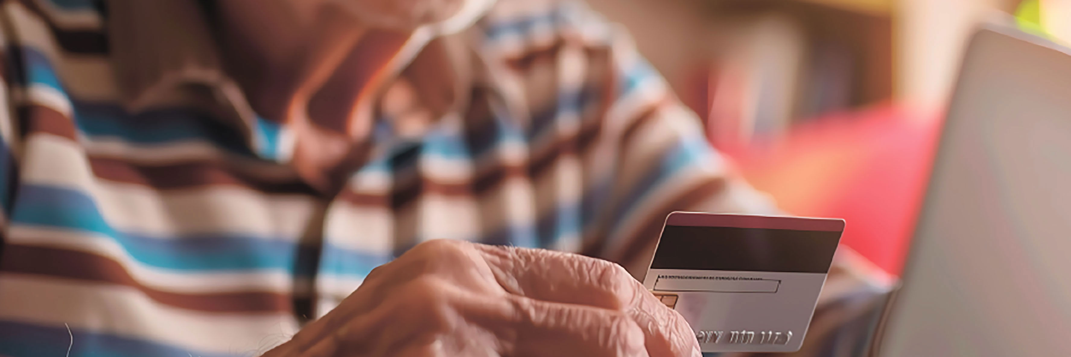 Ældre mand der holder et dankort op foran en PC