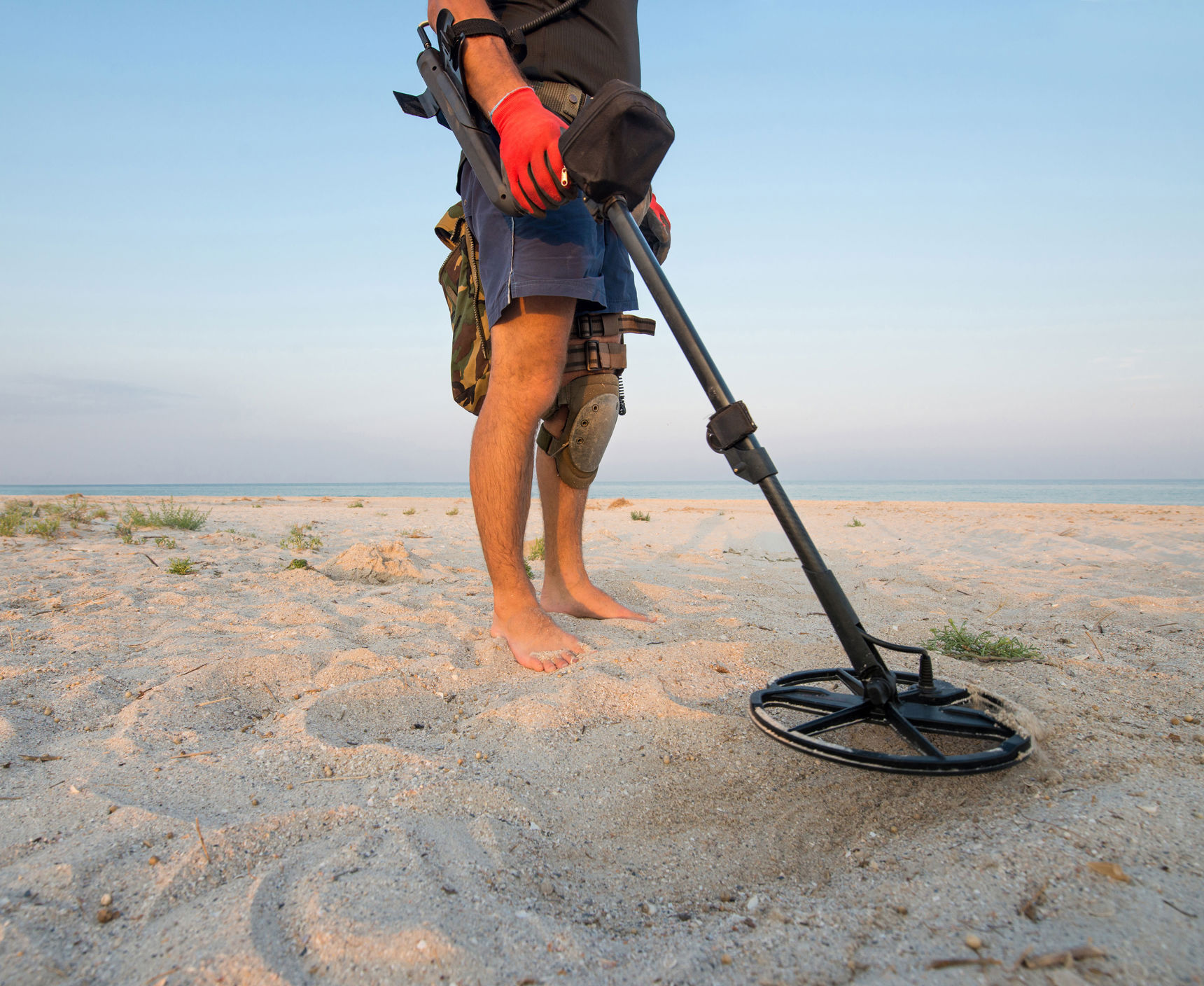 Mand der går på stranden med en metaldetektor