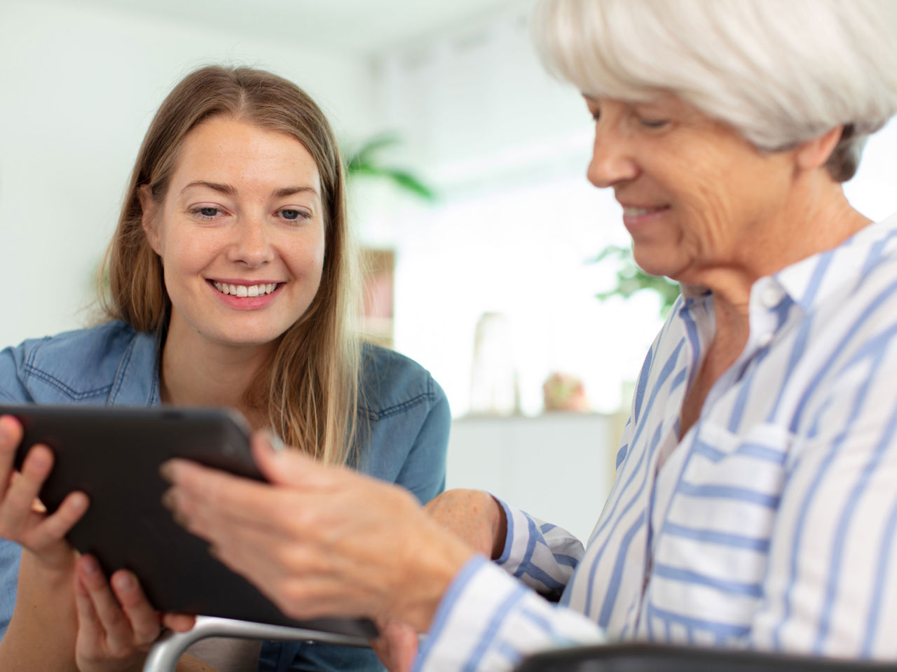 Yngre kvinde der hjælper en ældre kvinde med hendes iPad