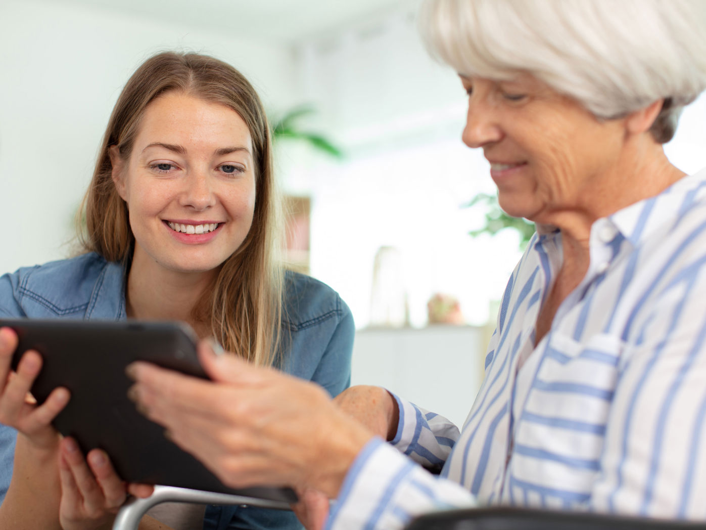 Yngre kvinde der hjælper en ældre kvinde med hendes iPad