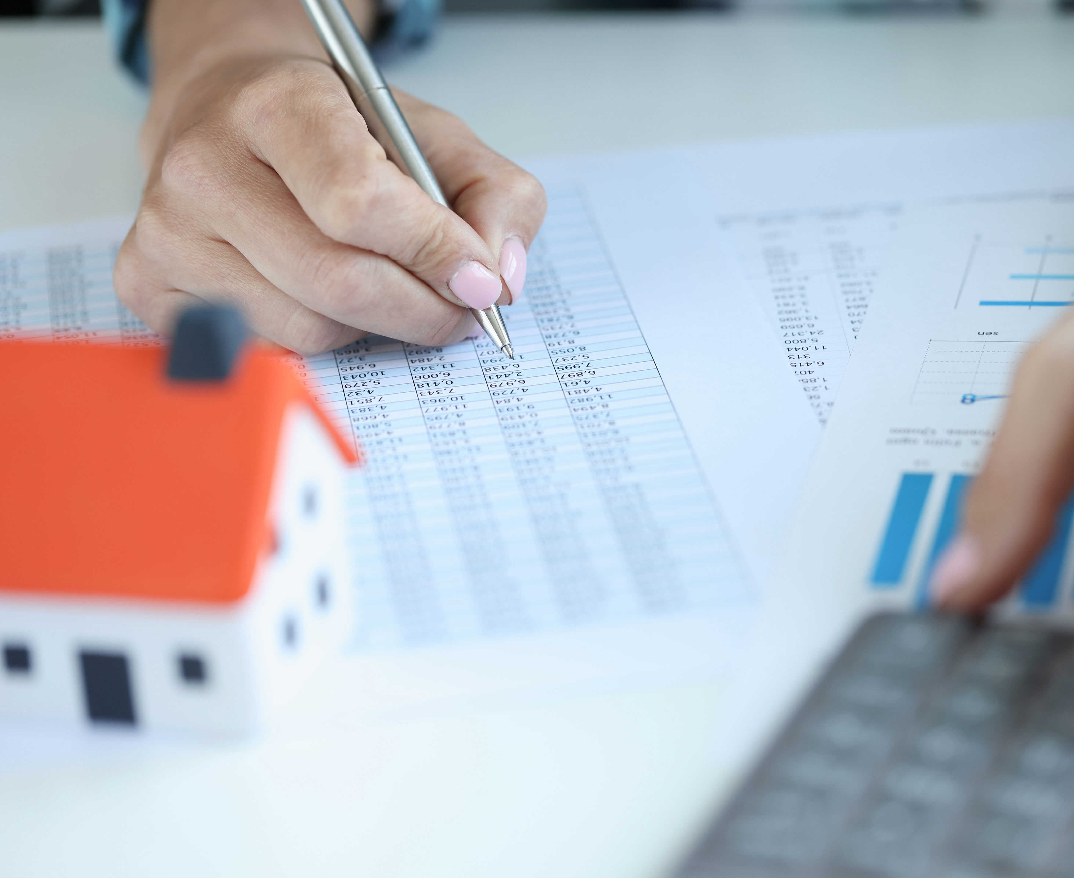 Hånd på et regneark med en lommeregner og et lille bitte hus foran sig