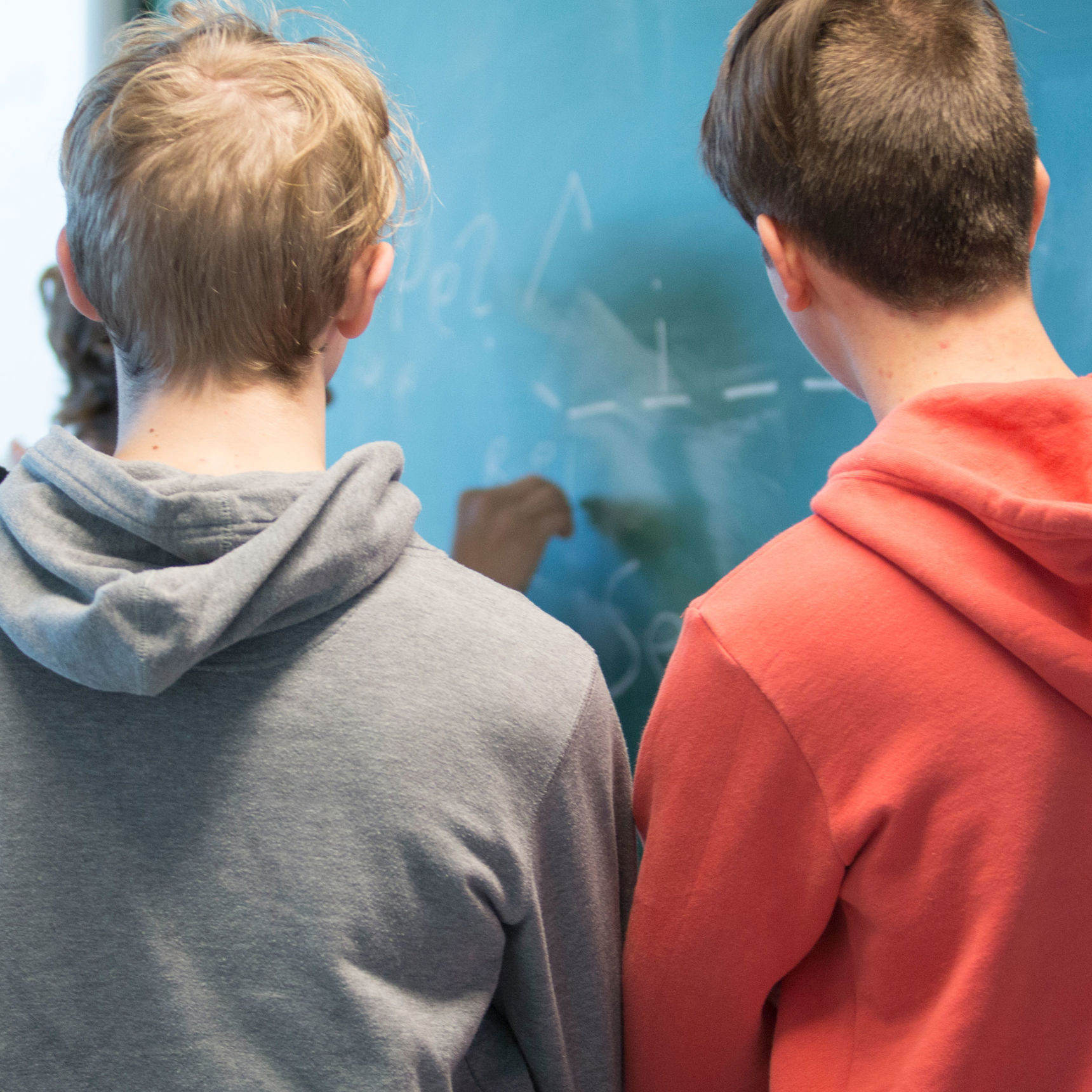 Tre skolelever med ryggen til der skriver på en tavle