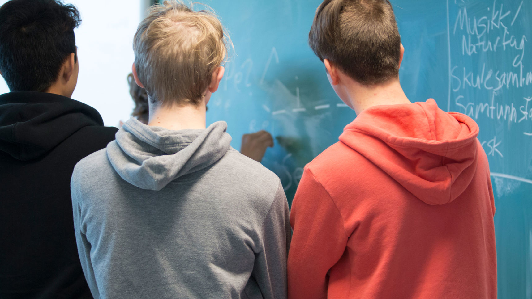 Tre skolelever med ryggen til der skriver på en tavle