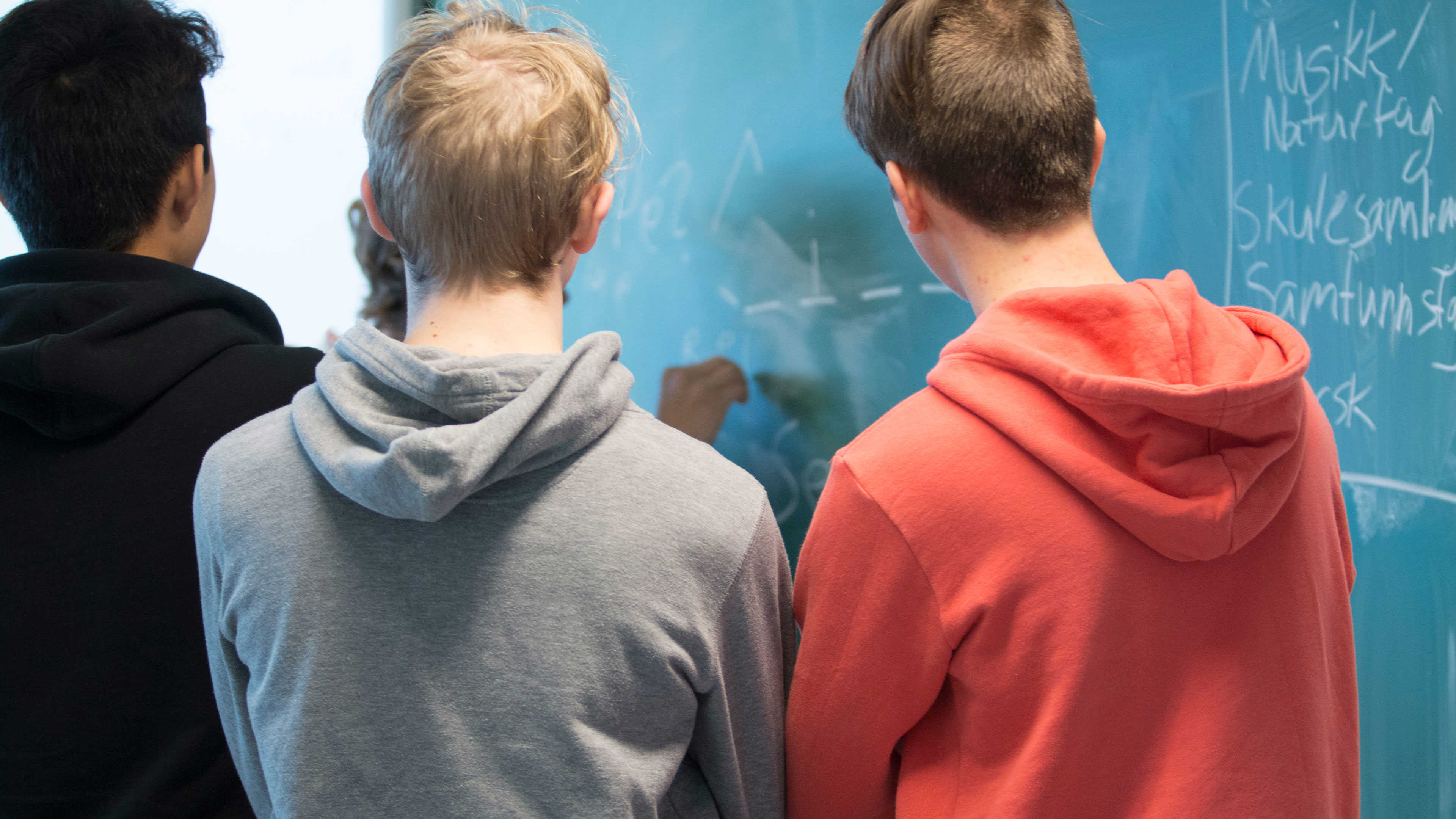 Tre skolelever med ryggen til der skriver på en tavle