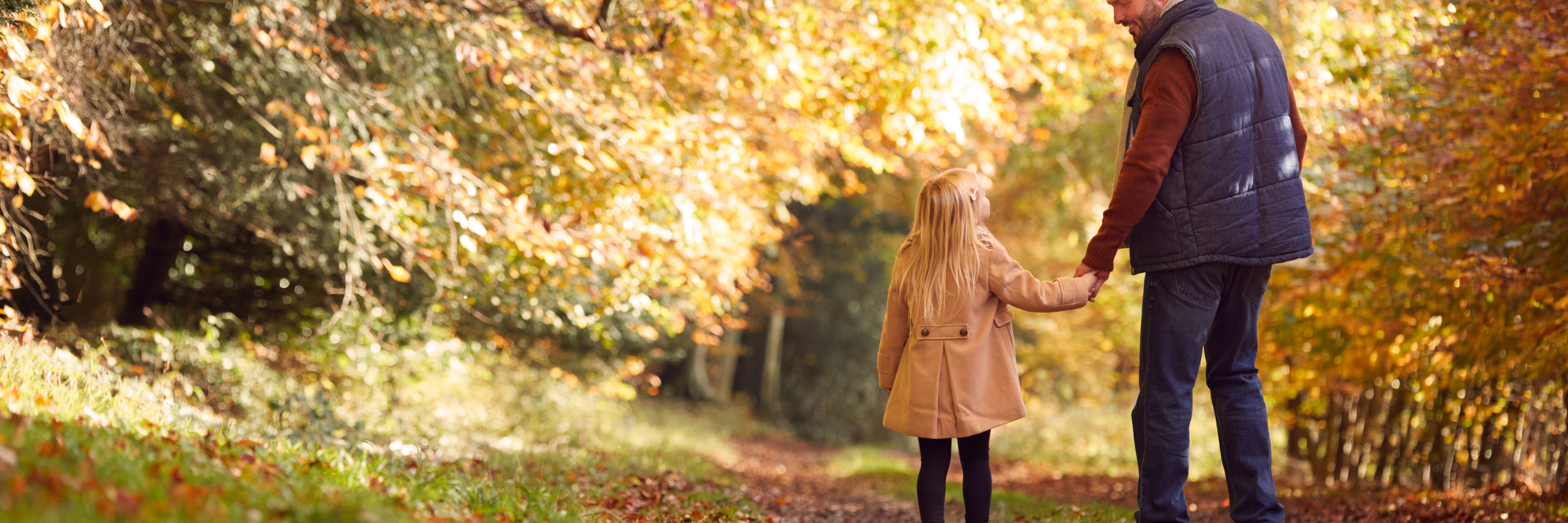 Mand holder barn i hånden i en efterårsskov