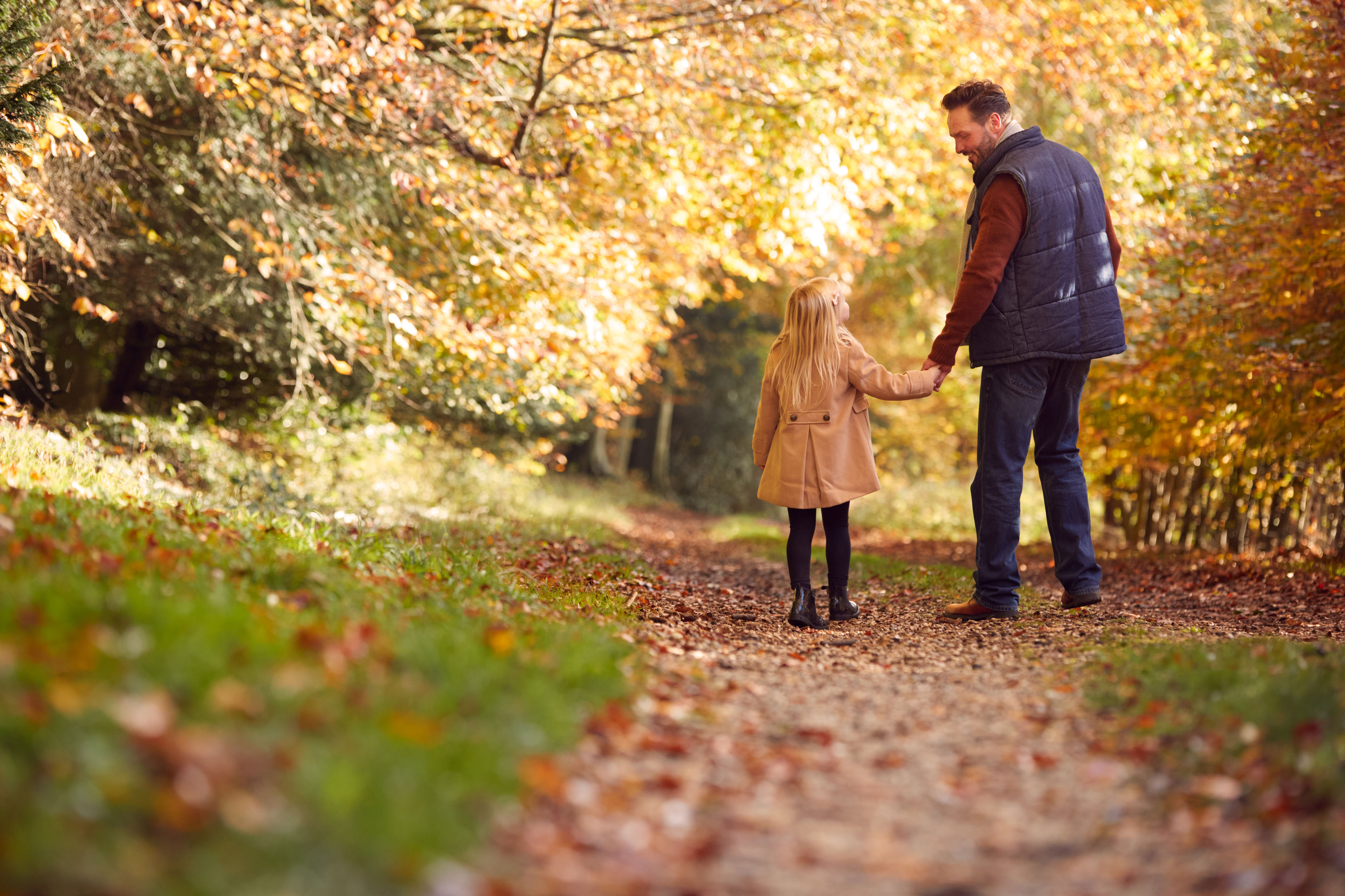 Mand holder barn i hånden i en efterårsskov