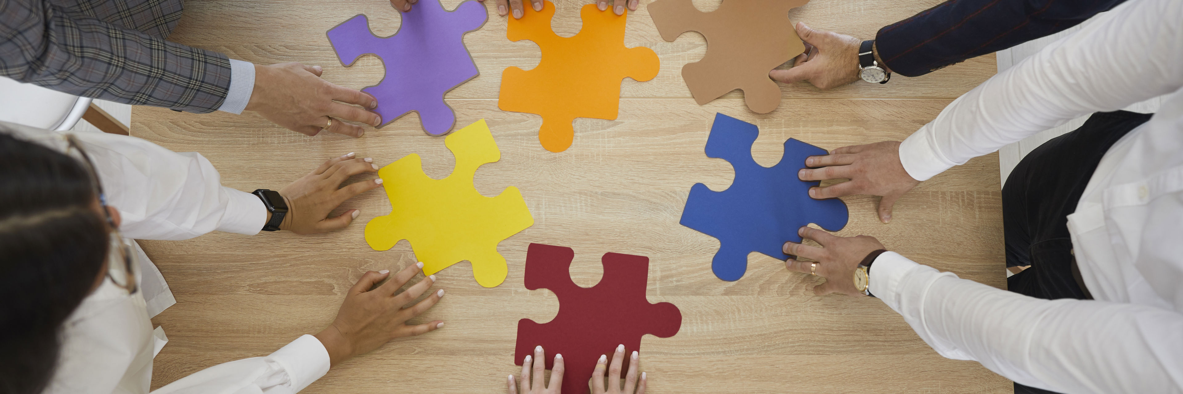 Hænder der hver holder en puslespilsbrik på et bord