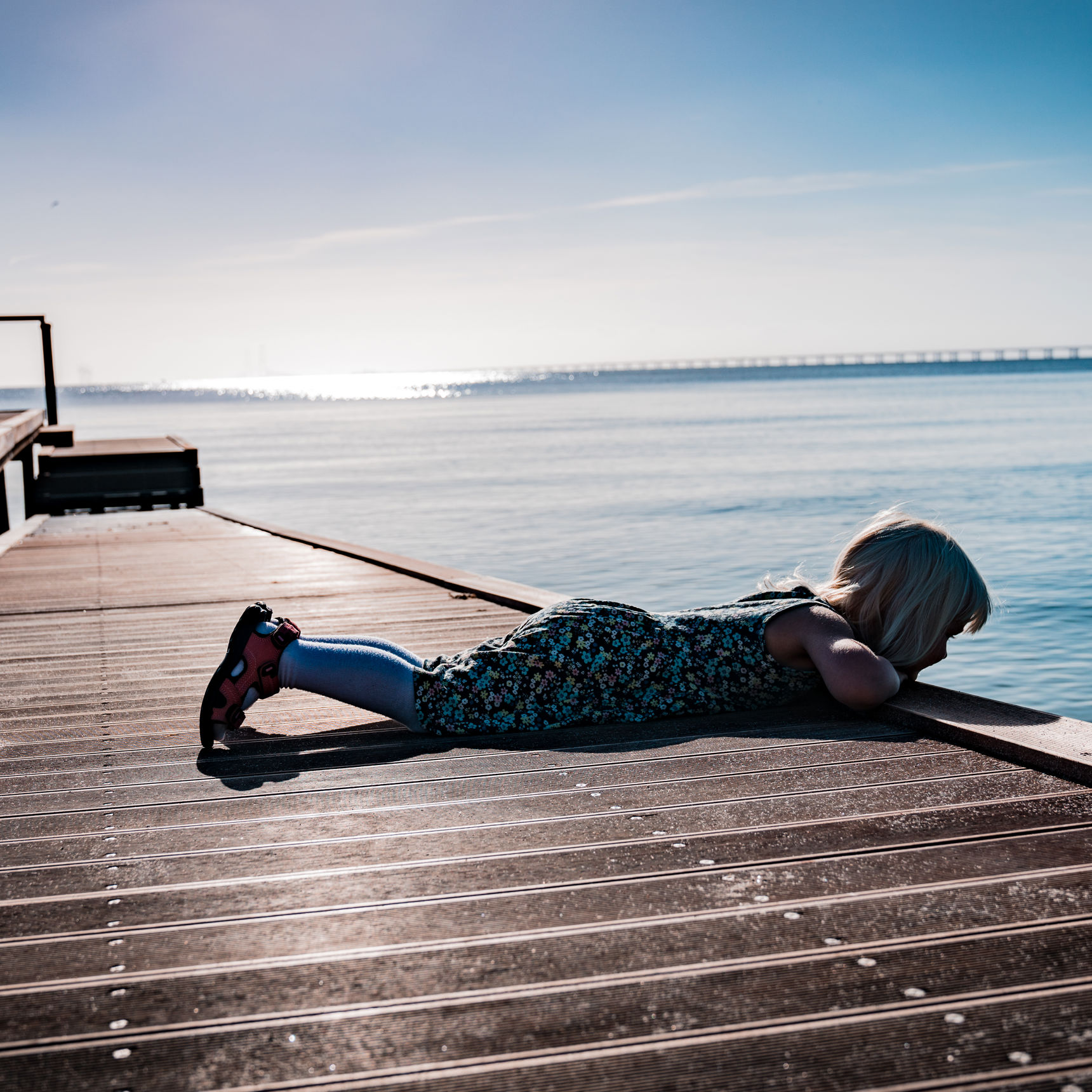 Pige der ligger på maven og kigger på vandet fra en badebro