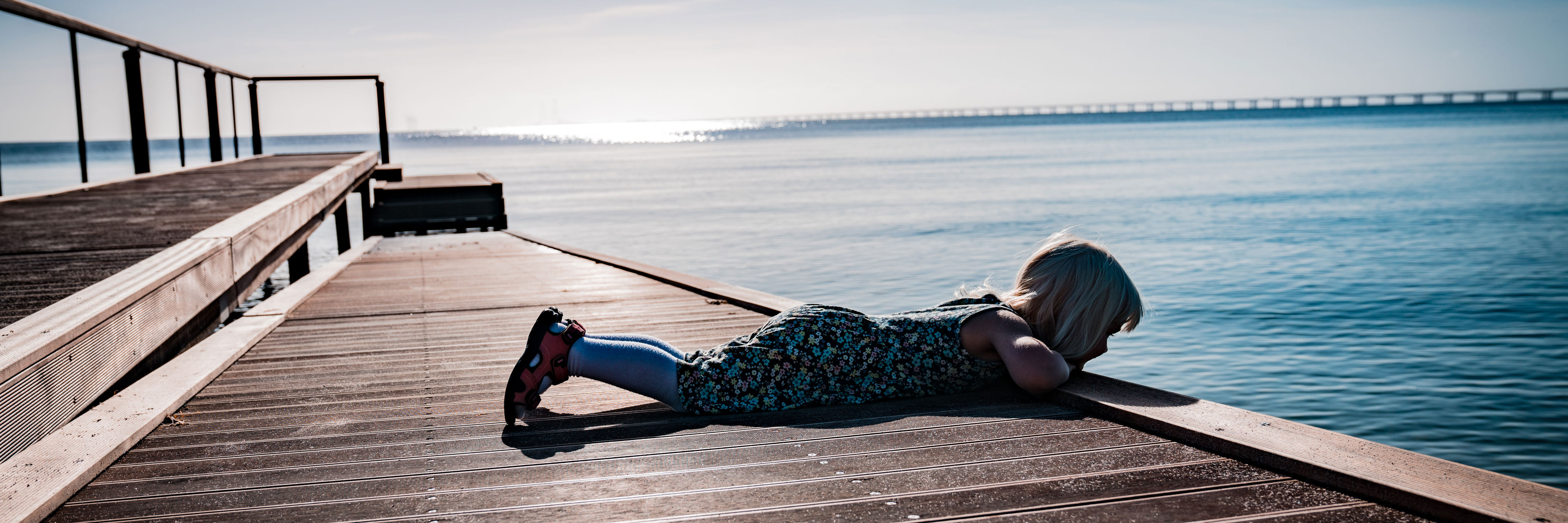 Pige der ligger på maven og kigger på vandet fra en badebro