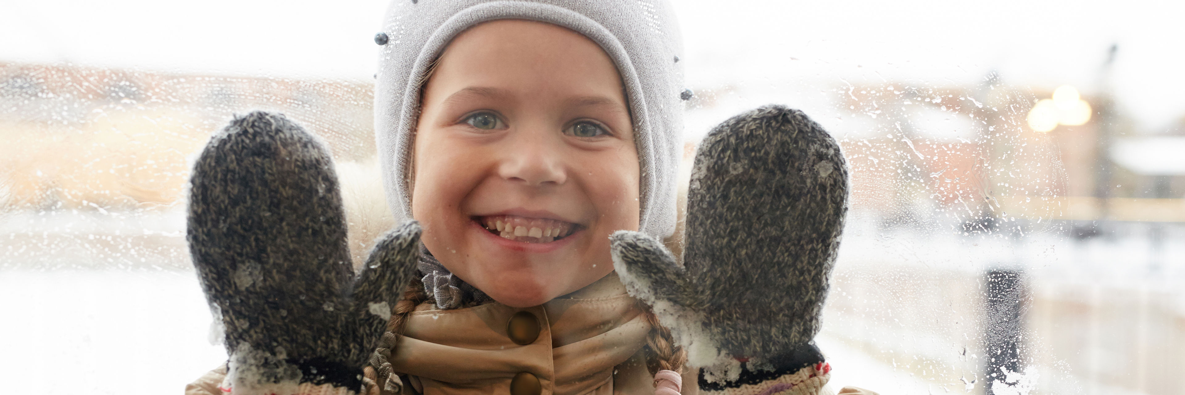Barn med hue og handsker der kigger gennem en rude