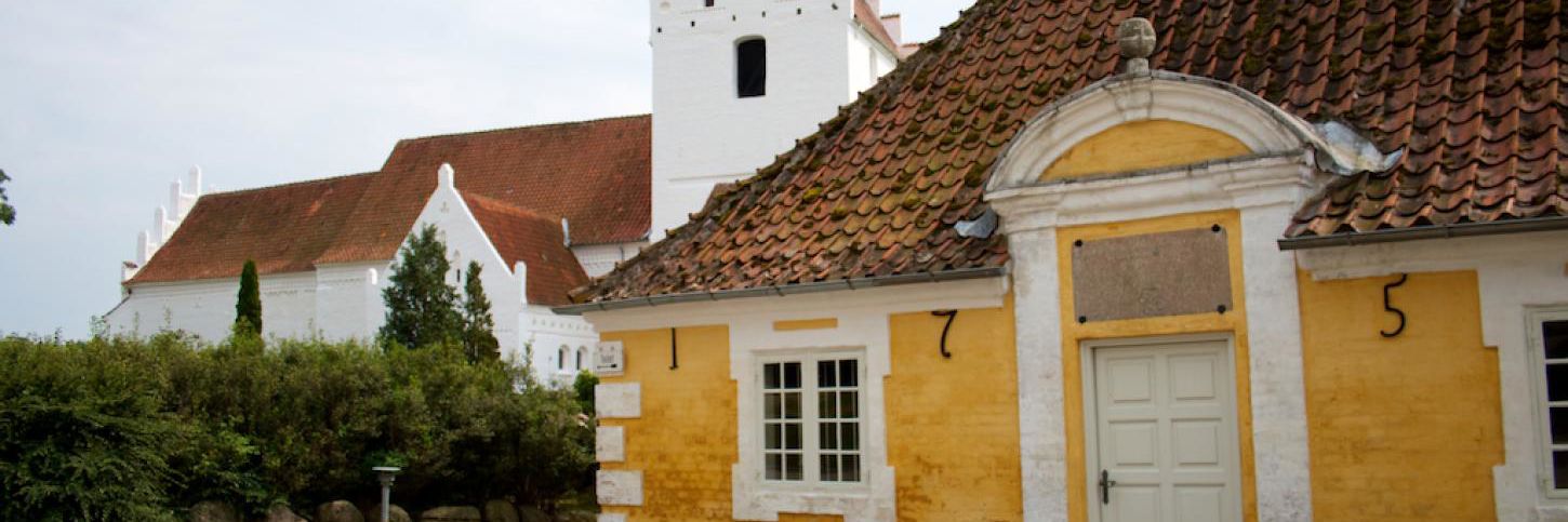 Aunslev Kirke med gul bygning i forgrunden